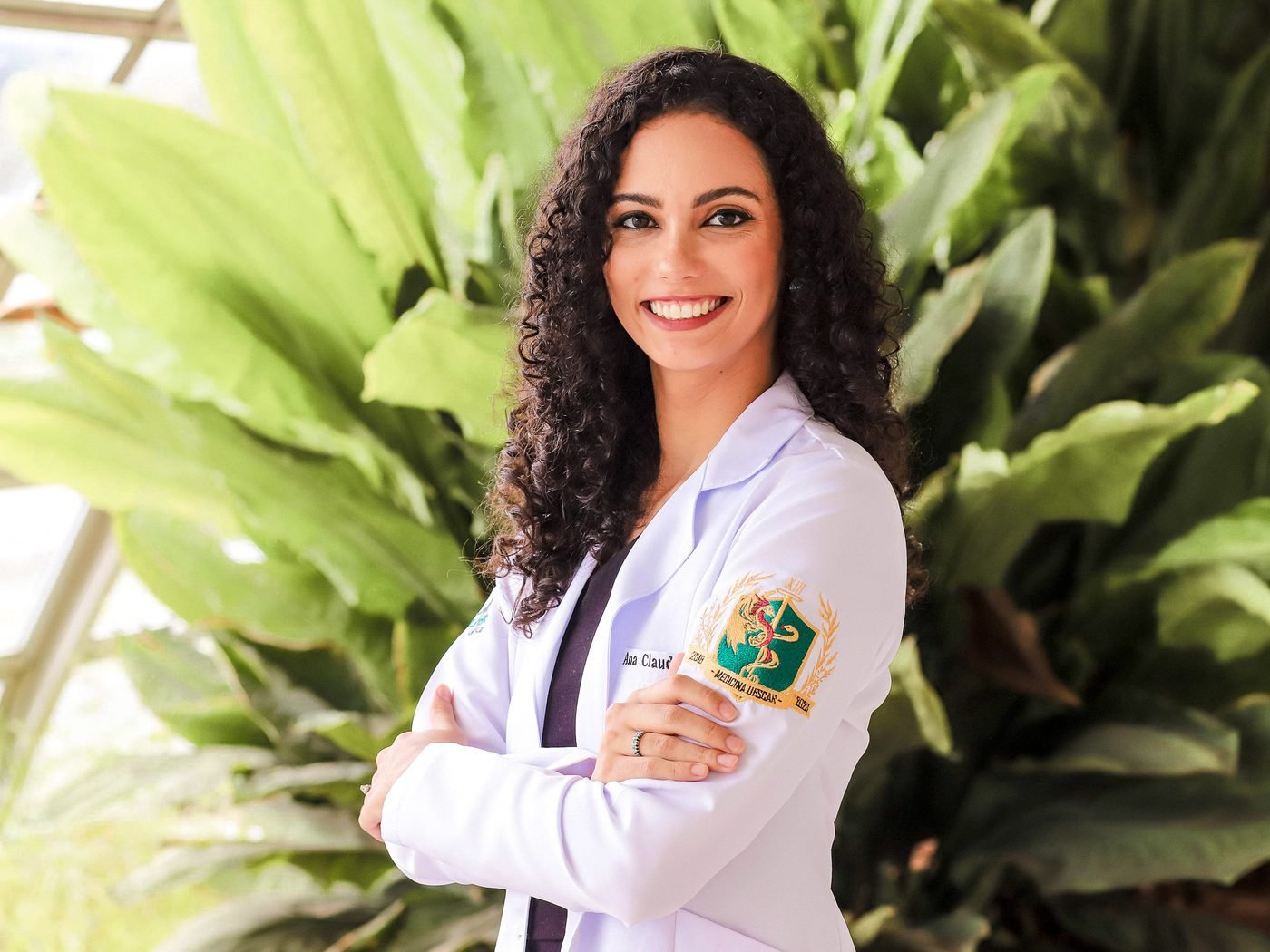 Dra. Ana Claudia sorrindo, de braços cruzados, entre plantas